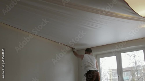 Static General plan of a young man installing a canvas of white stretch ceiling in the room of the apartment photo