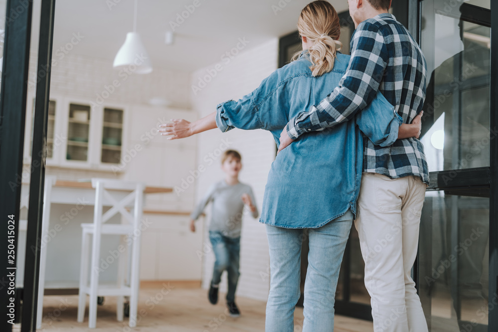 Fototapeta premium Rare view of couple hugging and their son running to them