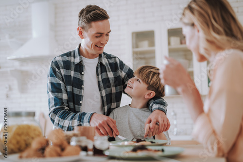 Positive man smiling to his son while cutting food with him