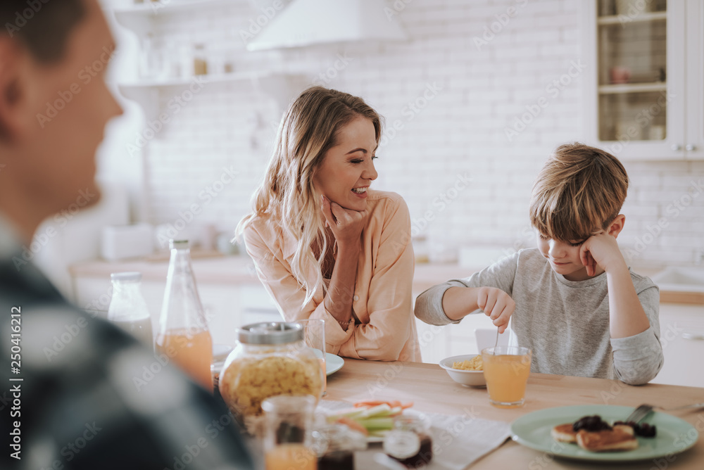 Boy eating breakfast and his mother smiling and looking at him Boy eating breakfast and his mother smiling and looking at him
