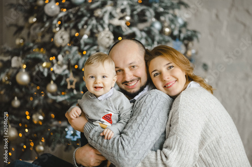 Christmas family portrait. Charming man  woman and their little son have fun posing before a Christmas tree in a bright room