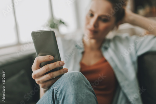 Relaxed female sitting on couch with smartphone