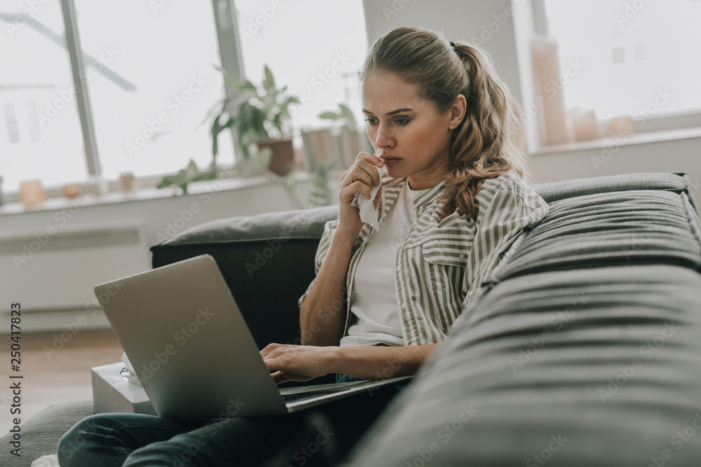 Tired woman with flu sitting on sofa with laptop Tired woman with flu sitting on sofa with laptop