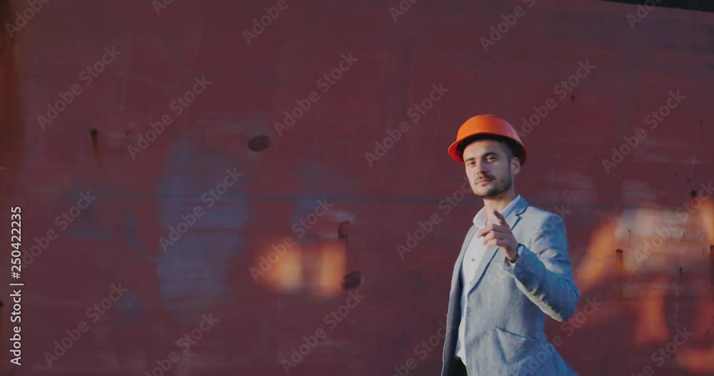 man in gray business suit and orange helmet appears in frame against brown blurry wall at sunset light man in gray business suit and orange helmet appears in frame against brown blurry wall at sunset light