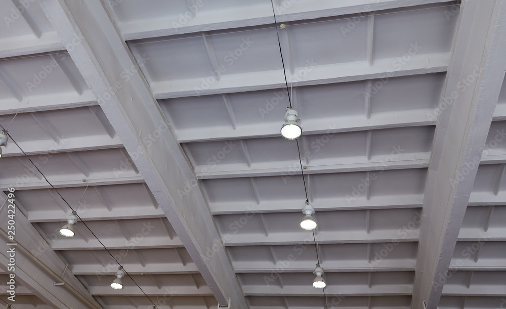 Turned-on warm tone light bulbs in lamps lined up under grey painted cement ceiling - rustic and loft style - open space - perspective worm view. Ceiling lighting in the gymnastics hall.