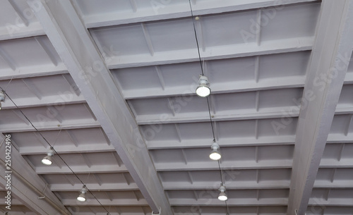 Turned-on warm tone light bulbs in lamps lined up under grey painted cement ceiling - rustic and loft style - open space - perspective worm view. Ceiling lighting in the gymnastics hall.