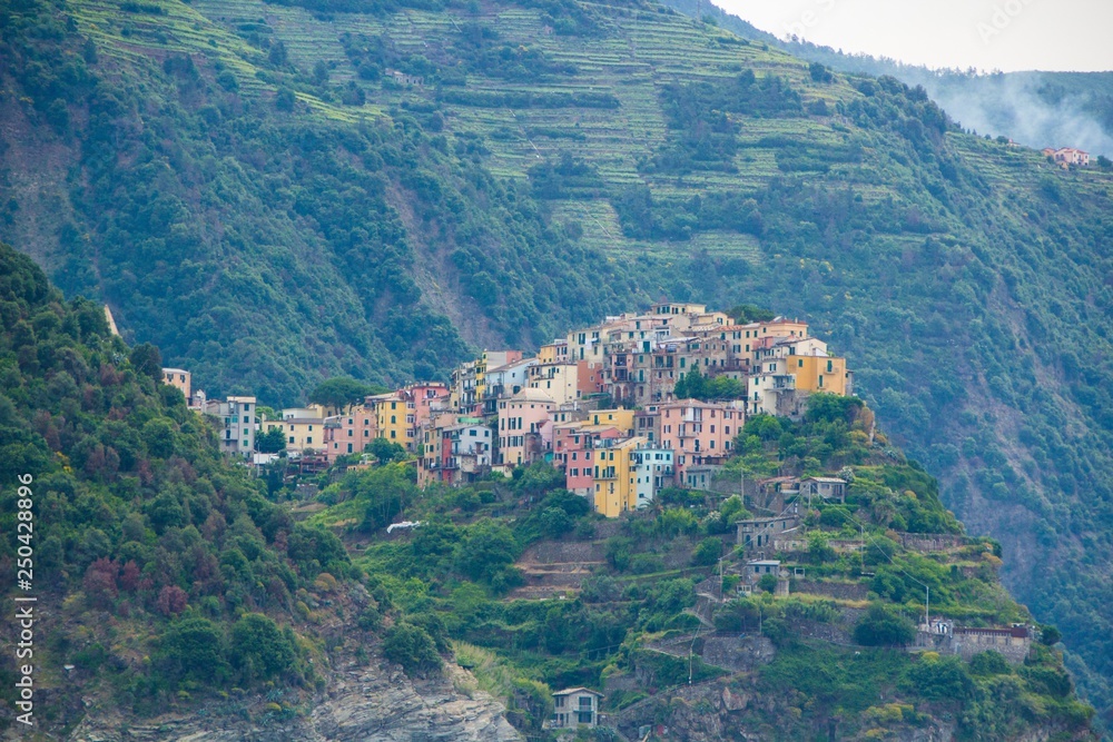 The town of Corniglia, one of the five small towns in the Cinque Terre national Park, Italy. View from the excursion ship. Amazing colorful small town located in the mountains near the sea.