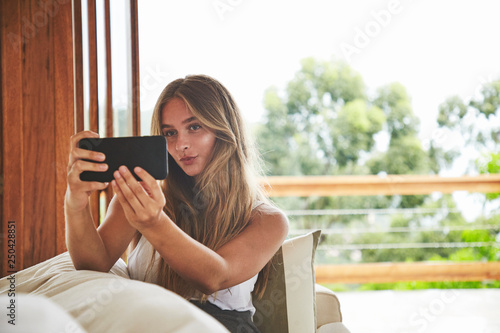 Young beautiful blond woman taking pouting selfie from sofa