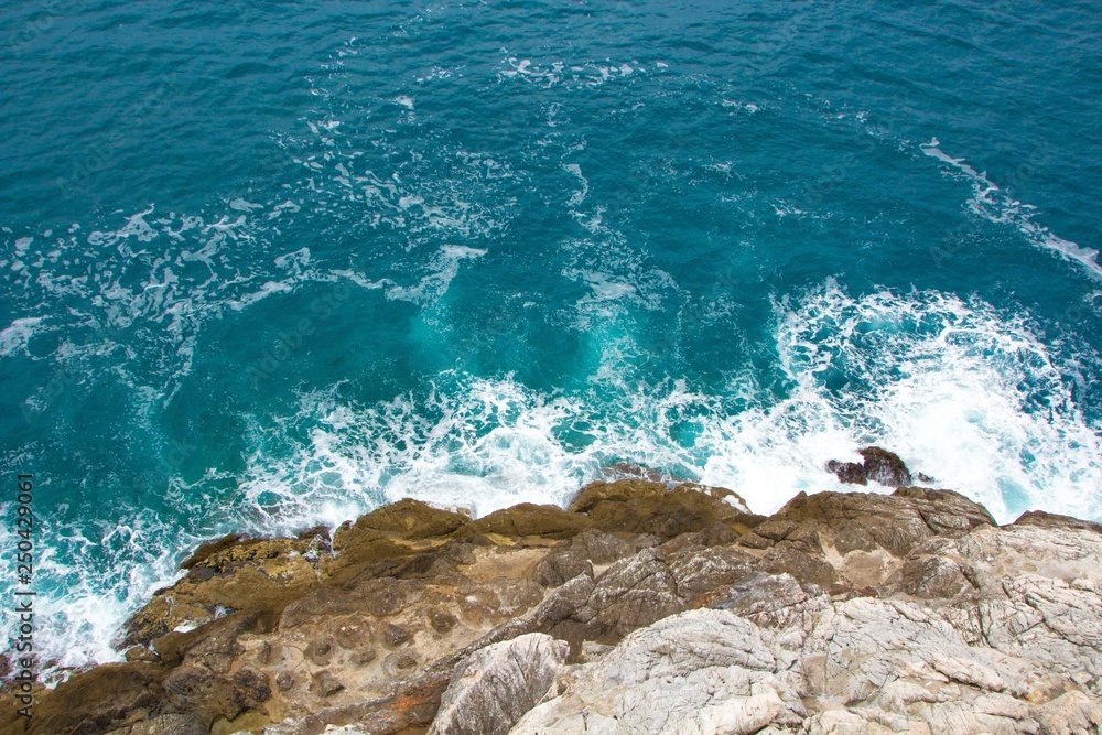 Fototapeta premium Azure blue sea waves crash on the rocks. Beautiful white foam spreads in all directions. Sea background. The view from the top.