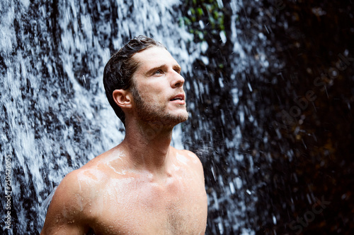 Young handsome guy under fresh waterfall