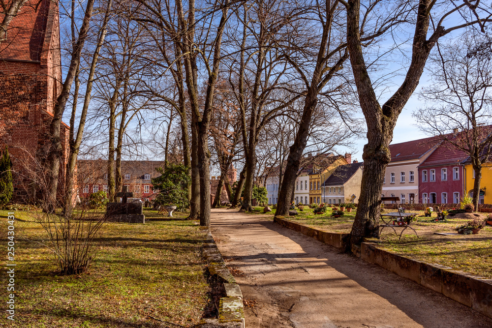 Germany, Brandenburg, Jueterbog: Public park garden of famous Liebfrauenkirche (Church of Our Lady) in the city center of the German small town with leafless trees, pathway, skyline and blue sky.