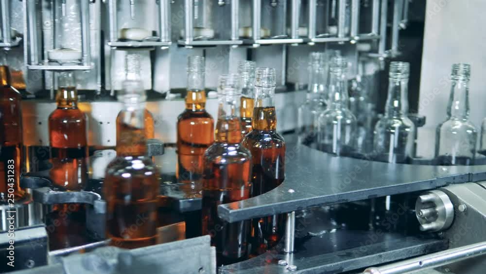 Whiskey, scotch, bourbon production. Automated machine filling bottles with alcohol at a factory. Whiskey, scotch, bourbon production. Automated machine filling bottles with alcohol at a factory.