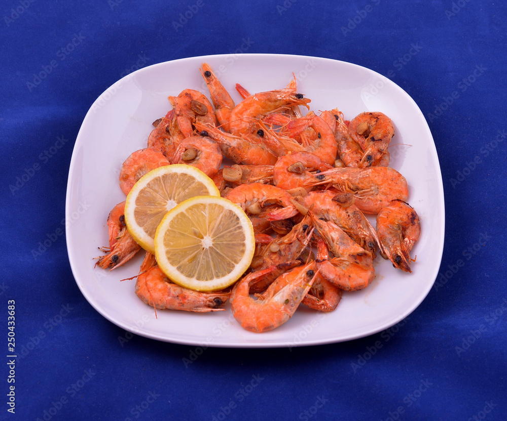 Red shrimps cooked with butter, garlic and lemon on white plate and blue background Red shrimps cooked with butter, garlic and lemon on white plate and blue background