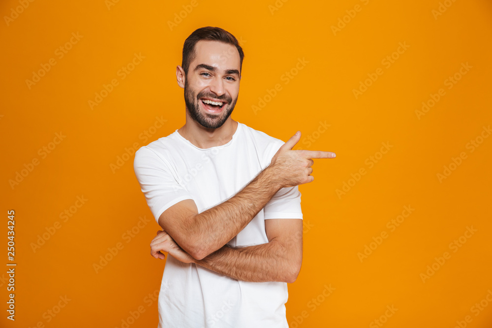 Image of bearded man 30s in t-shirt pointing finger aside while standing, isolated over yellow background Image of bearded man 30s in t-shirt pointing finger aside while standing, isolated over yellow background