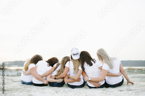 Bridal shower, hen party. Look from behind at charming girls in the same t-shirts and bride in the cap with lettering 'Bride'