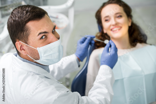selective focus of dentist in mask holding dental equipment during examination of female patient