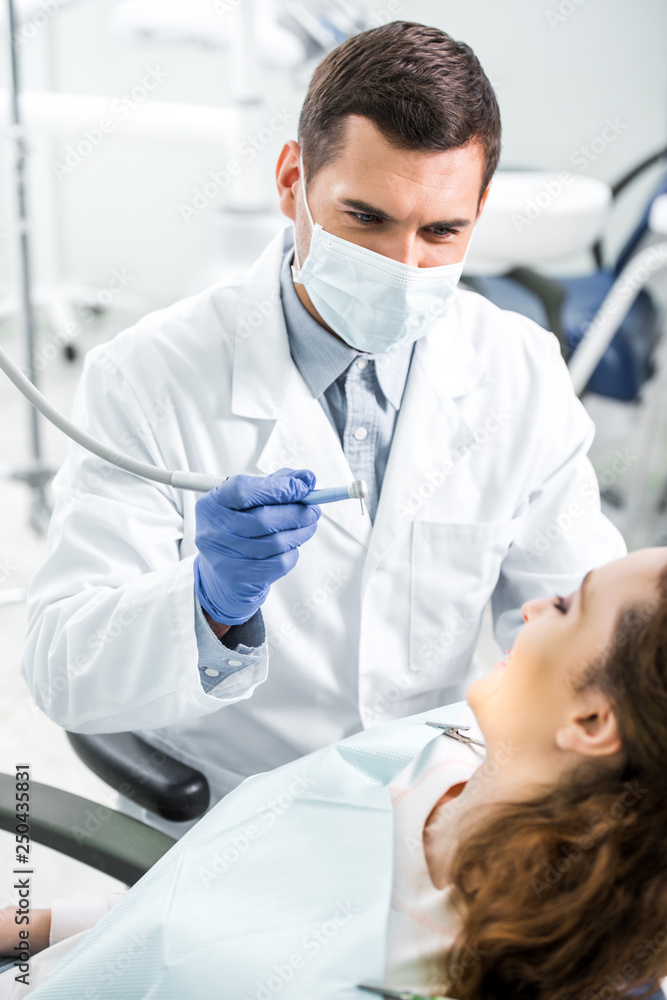 selective focus of dentist in white coat and mask holding dental instrument near female patient selective focus of dentist in white coat and mask holding dental instrument near female patient