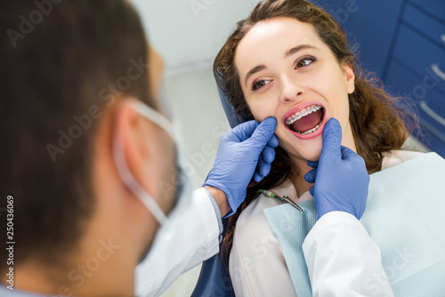 selective focus of woman in braces opening mouth during examination of teeth near dentist