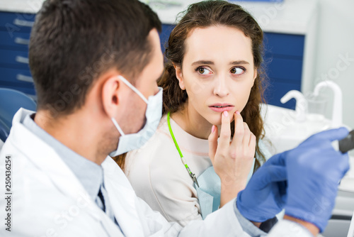 selective focus of pensive woman looking at dentist with x-ray of teeth in hands