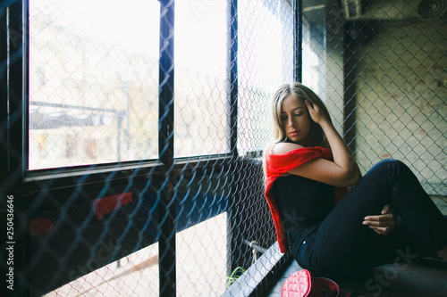 Streetstyle female portrait. Woman dressed in red shirt and sport pands sits in the dark room photo