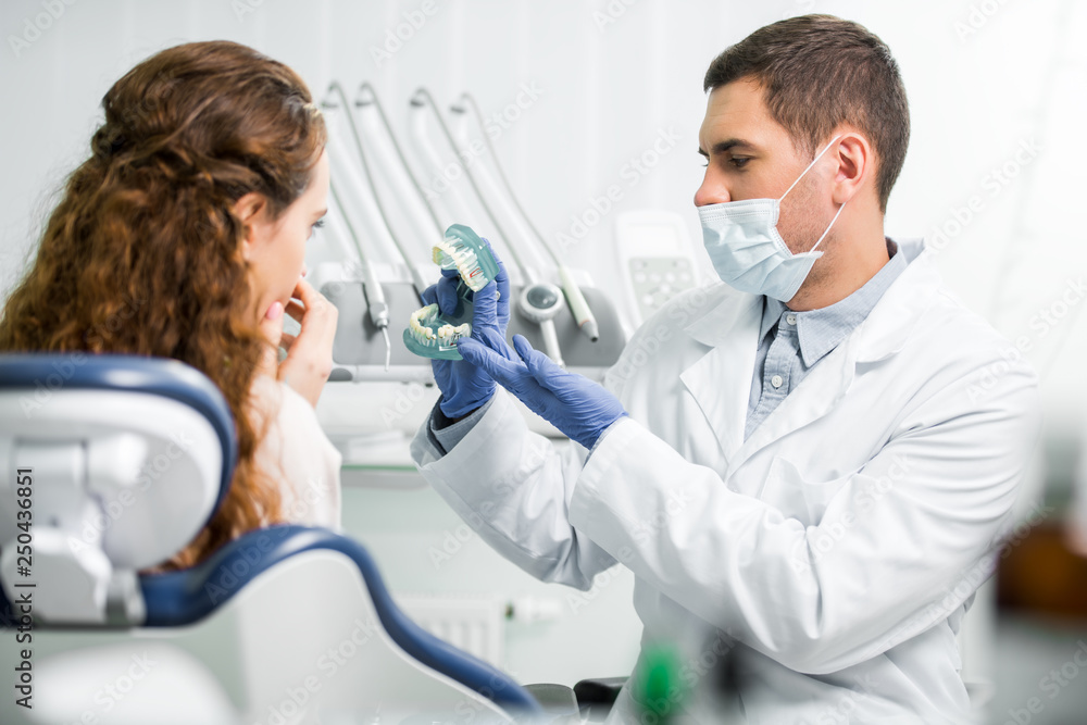 selective focus of dentist in latex gloves showing teeth model near female patient selective focus of dentist in latex gloves showing teeth model near female patient