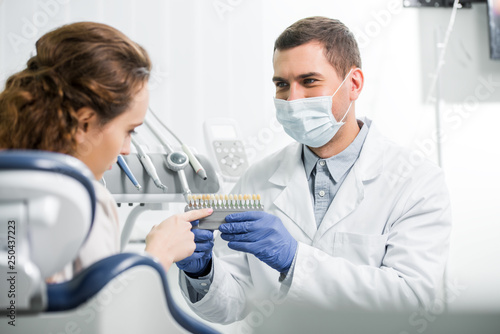 woman choosing teeth color palette near dentist in mask and latex gloves