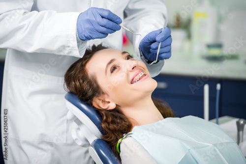 cropped view of dentist in latex gloves examining cheerful woman in braces