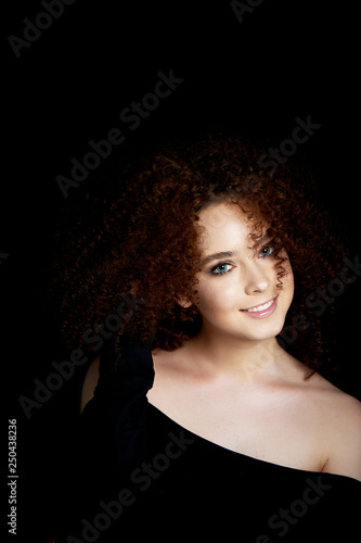 A girl with lush curly red hair. Open shoulders. Corrects hair and smiles