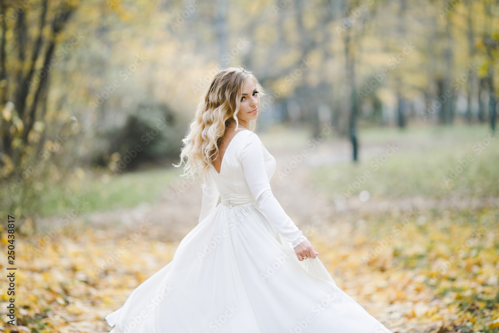 Look from behind at charming bride whirling in autumn park covered with fallen leaves