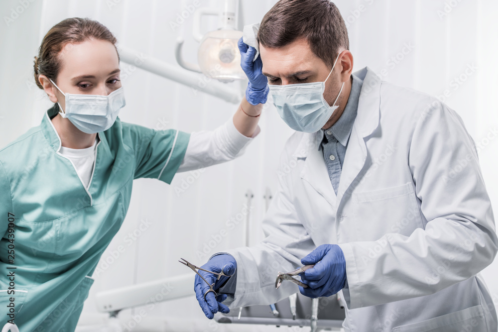 female dentist in mask standing near colleague holding dental instruments female dentist in mask standing near colleague holding dental instruments