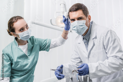 female dentist in mask looking at colleague holding dental instruments