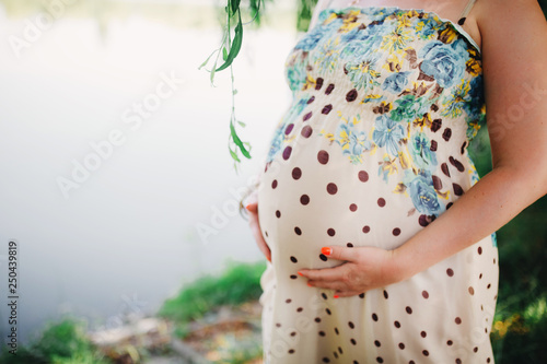 Silhouette of a pregnant woman in a beautiful dress on a light background. Focus on the abdomen.