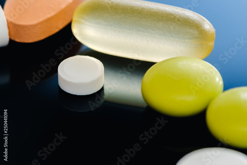 Heap of capsule pills tablets medicine lying isolated on black background extreme close-up.
