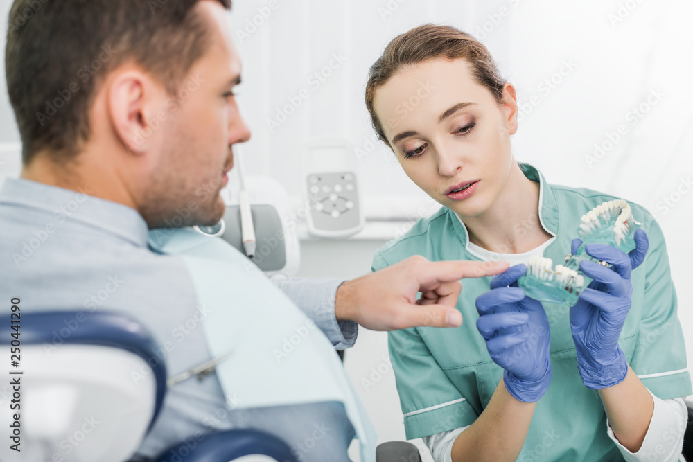selective focus of man pointing with finger at teeth model near beautiful dentist selective focus of man pointing with finger at teeth model near beautiful dentist