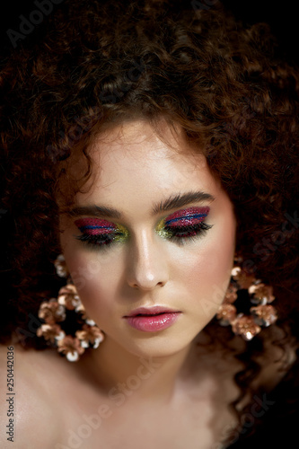 A girl with lush curly red hair. Close face with bright make-up and massive earrings.Purple shadows.