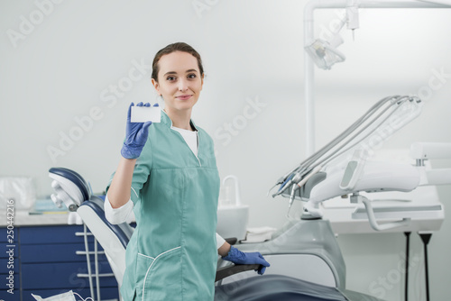 beautiful dentist holding blank card while standing in dental clinic