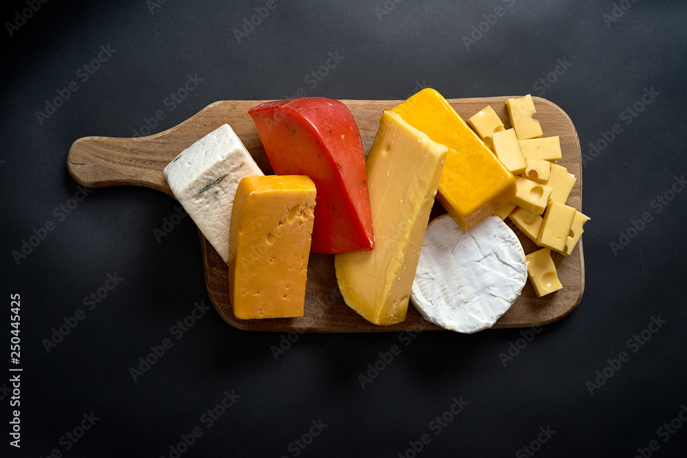 Fototapeta premium Wooden board with different kinds of cheeses on black table