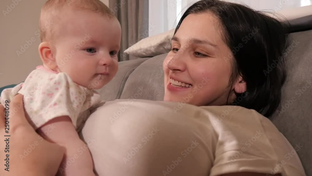 Woman Mother play with her little Baby Girl lying on a Sofa at Home Woman Mother play with her little Baby Girl lying on a Sofa at Home