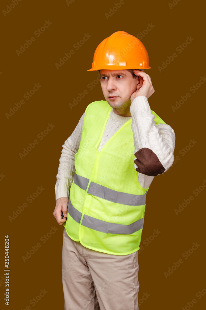 the man in a construction helmet, a vest laid a hand to an ear better to hear