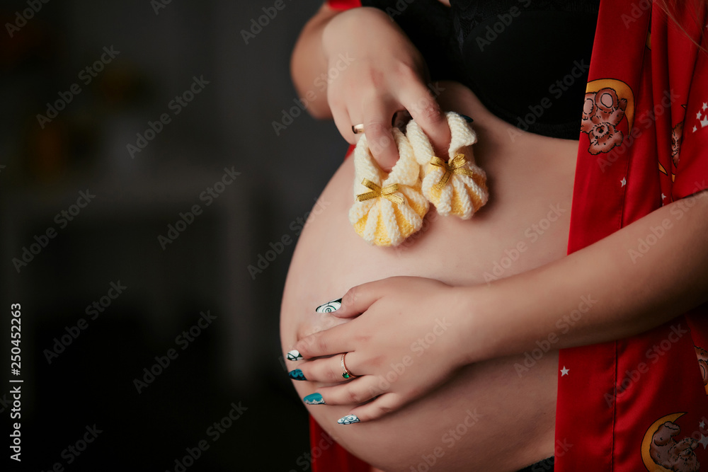 Obraz premium Happy pregnant female with big belly hold baby shoes