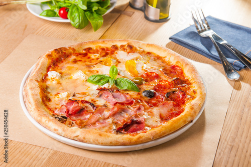 Delicious Meat Pizza with bacon and sausages on white plate on the wooden table with cutlery and ingredients. Selective focus, Copy space.