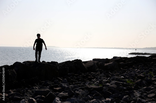 silhouette of teenage boy playing on the rocks at the beach