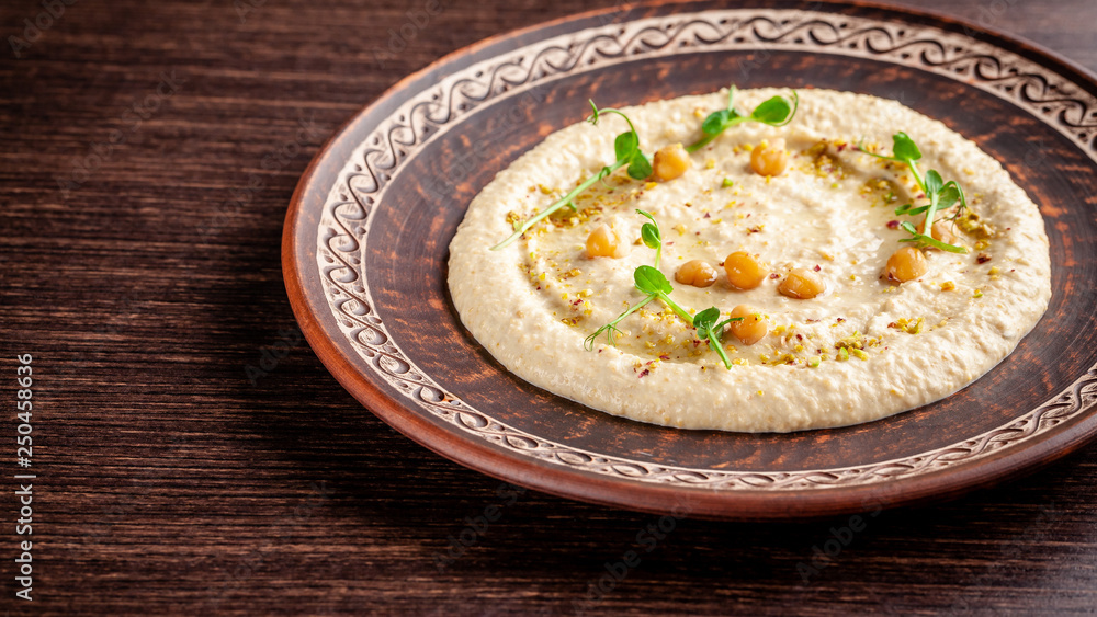 The concept of Arabic cuisine. Oriental hummus with grilled sesame and pistachios. A dish in a restaurant in a red ceramic dish on a wooden table. Top view, copy space The concept of Arabic cuisine. Oriental hummus with grilled sesame and pistachios. A dish in a restaurant in a red ceramic dish on a wooden table. Top view, copy space
