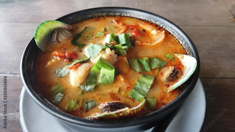 Thai Tom Yum Kung with some seafood ingredients served on wooden table. Thai Tom Yum Kung with some seafood ingredients served on wooden table.