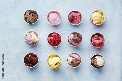 Scoops of fruits and chocolate ice cream in cups on rustic background, top view