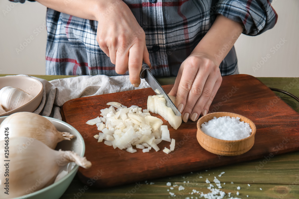 Woman cutting raw onion on table