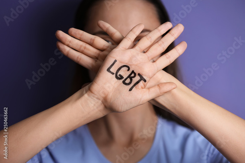 Young woman with written LGBT abbreviation on her palm against color background, closeup