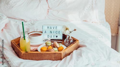 Breakfast in bed with Have a nice day text on lighted box. Coffee cup, juice, macaroons, flower in vase on wooden tray. Good morning mood. Hospitality, care, service concept. Wide banner. Copy space.