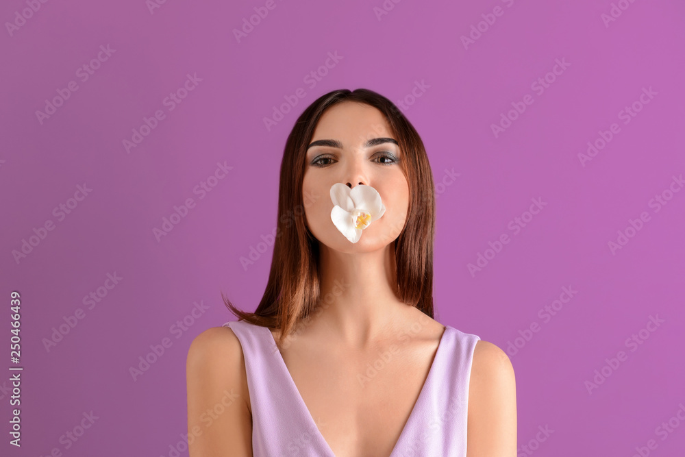 Beautiful young woman with orchid flower in mouth on color background Beautiful young woman with orchid flower in mouth on color background