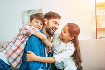 Handsome father is playing and have a fun with his little son and daughter at home on the couch. Happy family. Best father